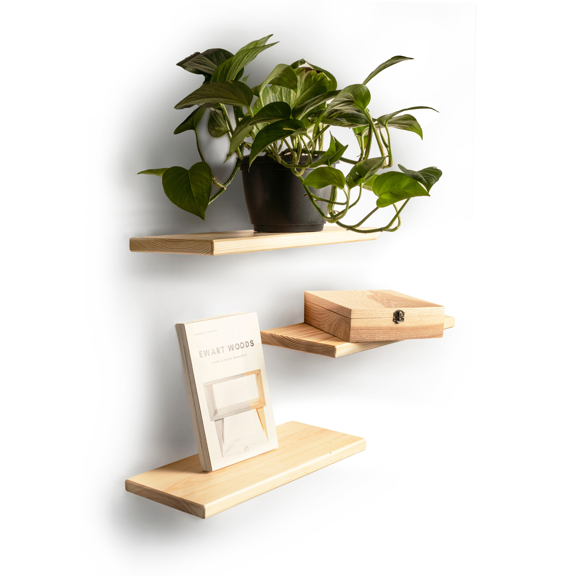 Set of three floating light wood shelves with rounded edges and visible wood grain. The top shelf holds a potted plant, the middle shelf has a wooden box with a latch, and the bottom shelf displays a book titled 'EWART WOODS.